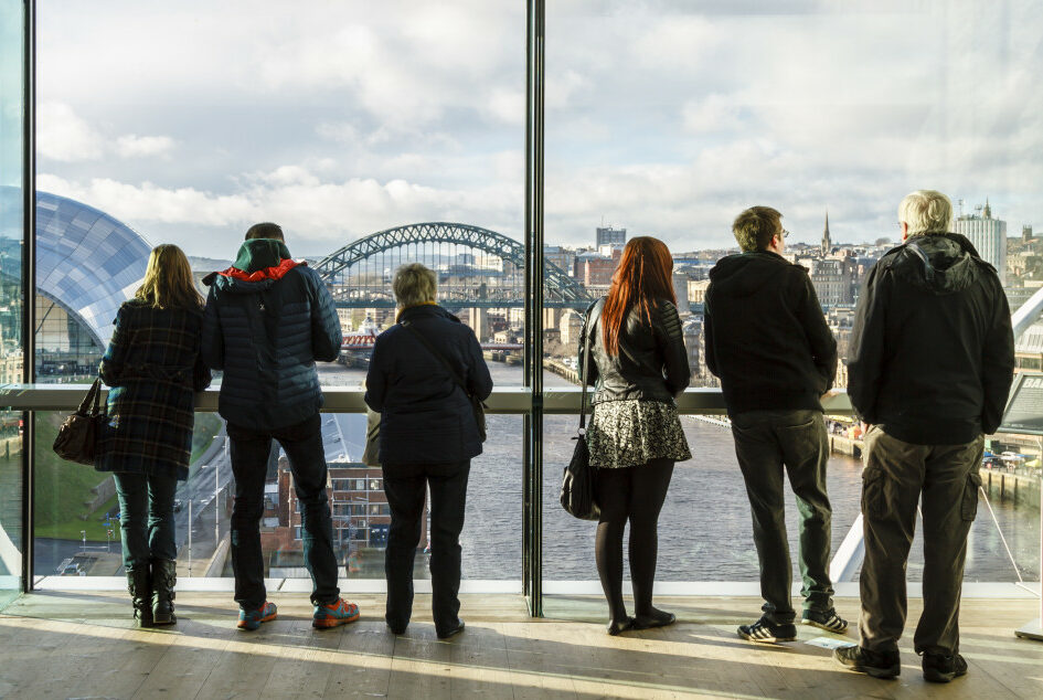 City view Newcastle upon Tyne bridge tourist attraction. People from behind looking through window.